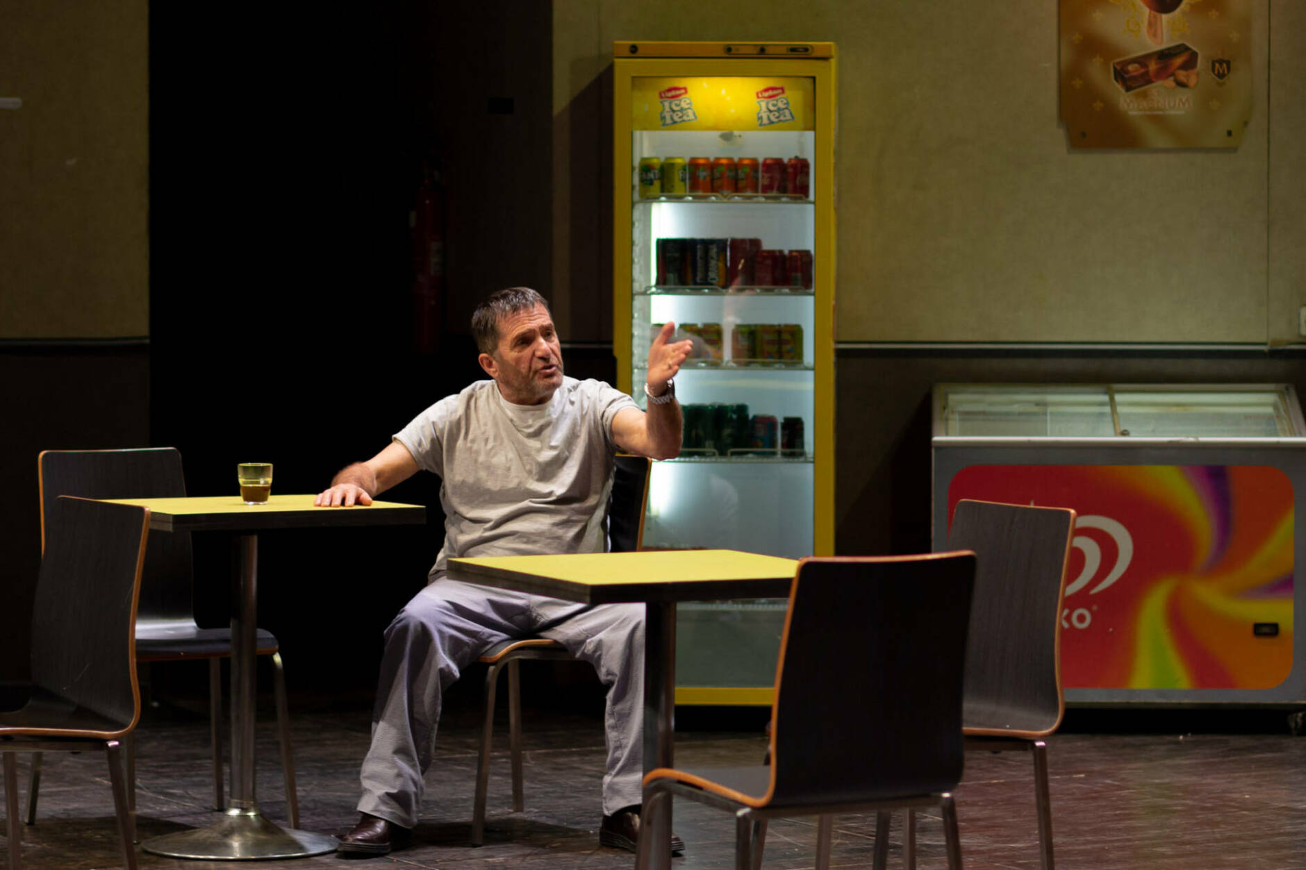 Un comédien assis à une table dans le spectacle Marius de Joël Pommerat